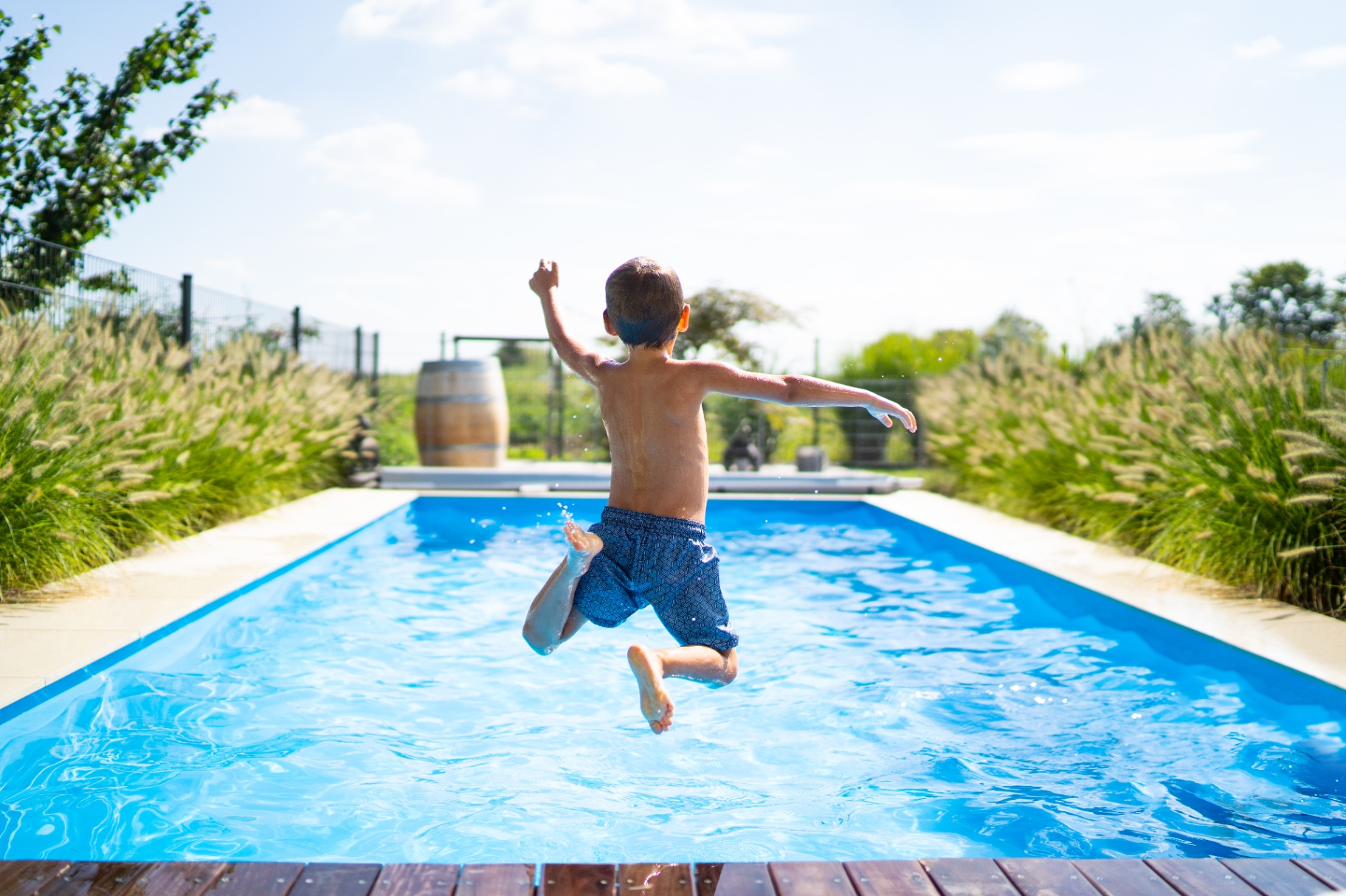 Child leaping into a backyard pool surrounded by ornamental grasses on the North Fork of Long Island.